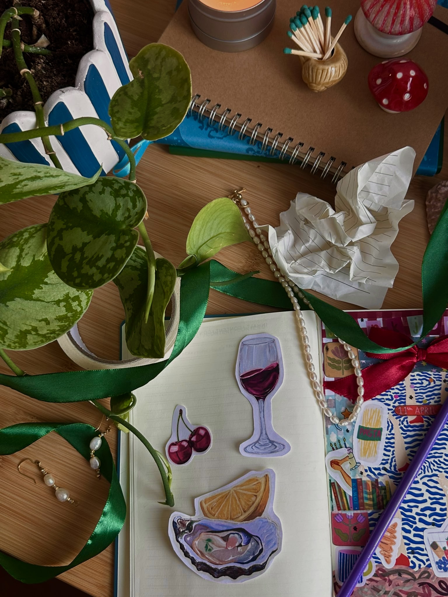 A scrapbook page with hand-drawn food and wine motifs beside ribbons, plants and creative materials