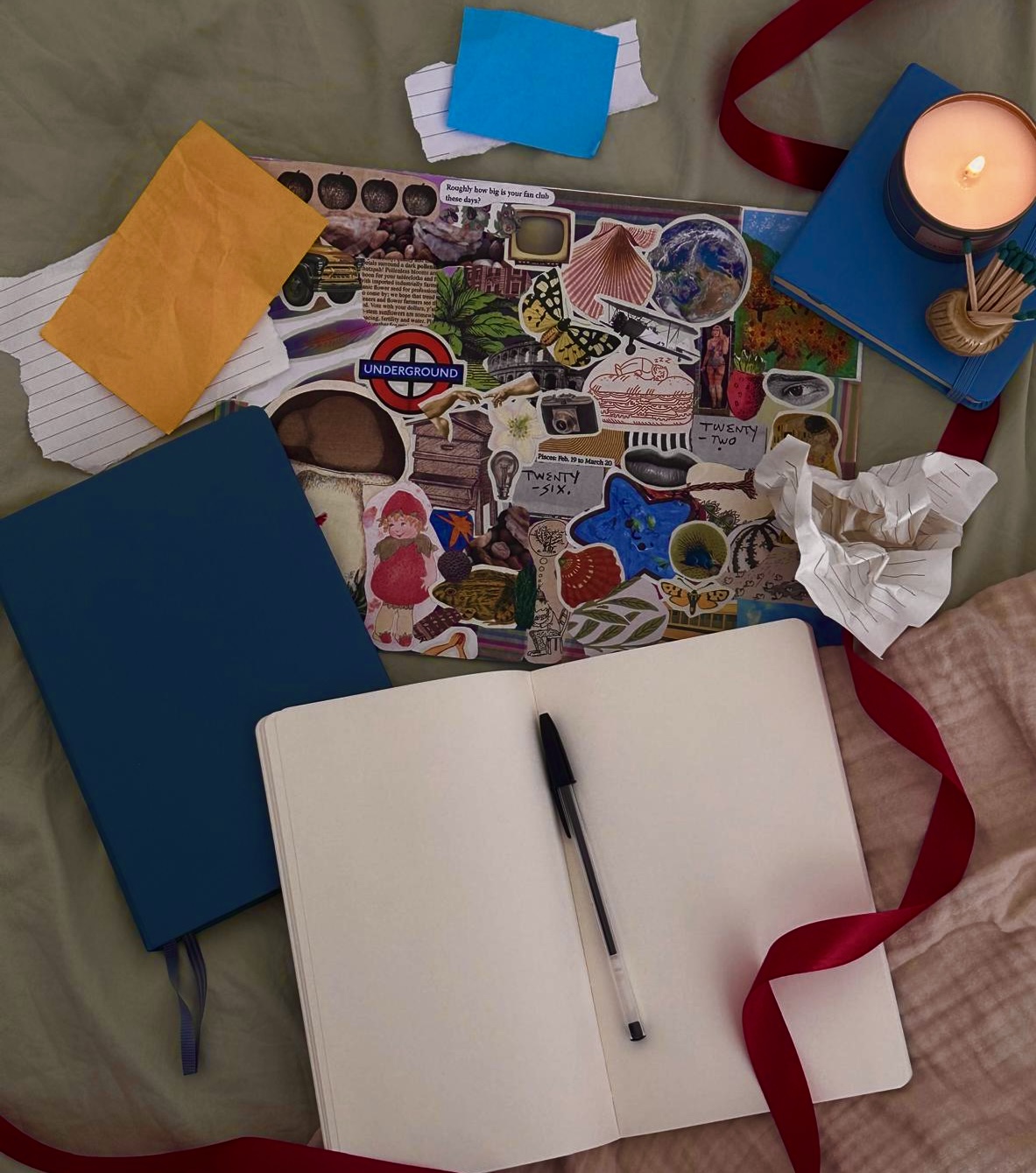 An open notebook beside scrapbook cut-outs, ribbons and a candle